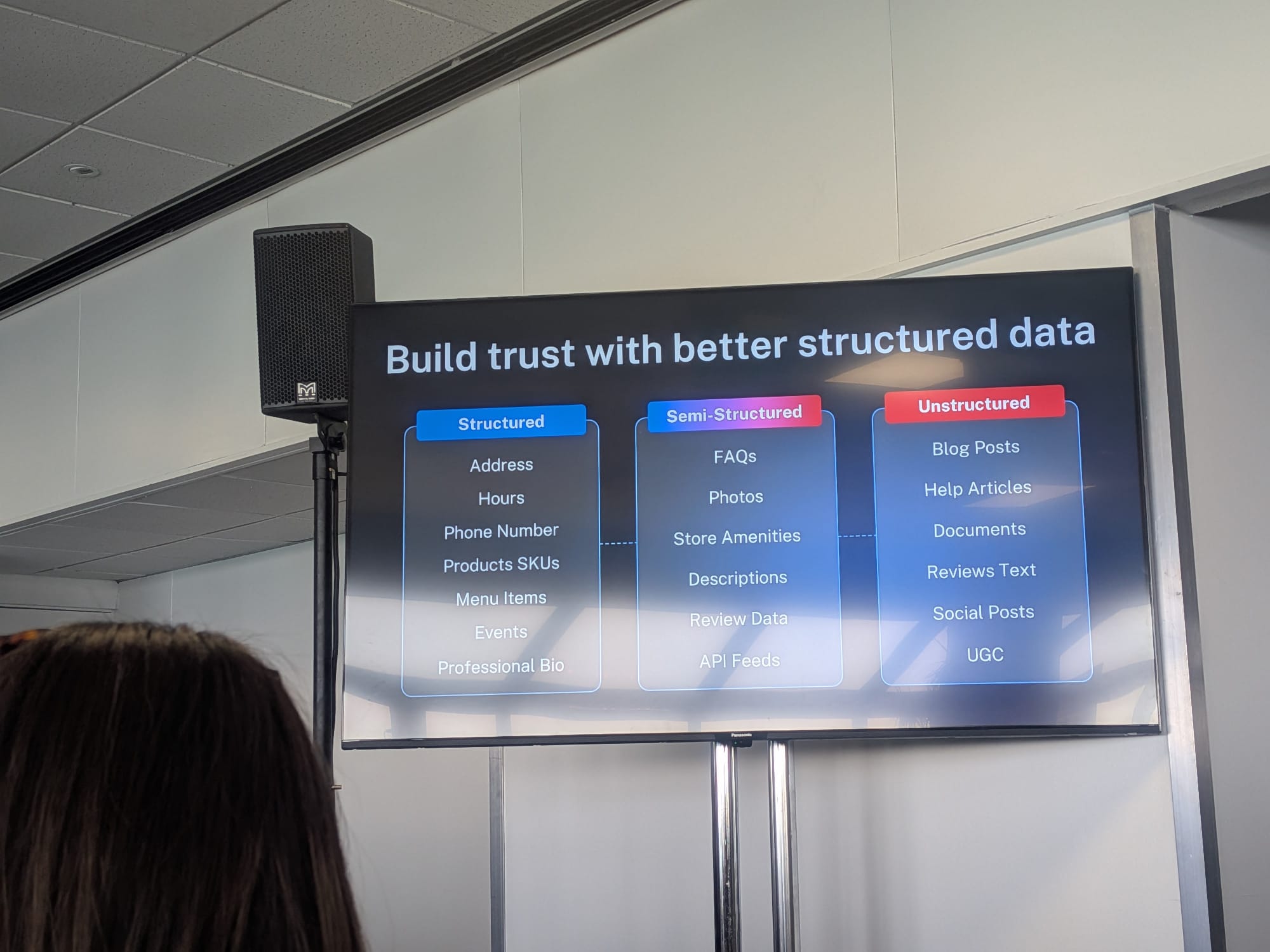 Wendi SturgisのBrightonSEO 2026セッションのスライド「Build trust with better structured data」: 3つの列 — Structured(住所、営業時間、電話番号、商品SKU、メニュー項目、イベント、プロフェッショナルバイオ)、Semi-Structured(FAQ、写真、店舗アメニティ、説明、レビューデータ、APIフィード)、Unstructured(ブログ記事、ヘルプ記事、ドキュメント、レビューテキスト、ソーシャル投稿、UGC)