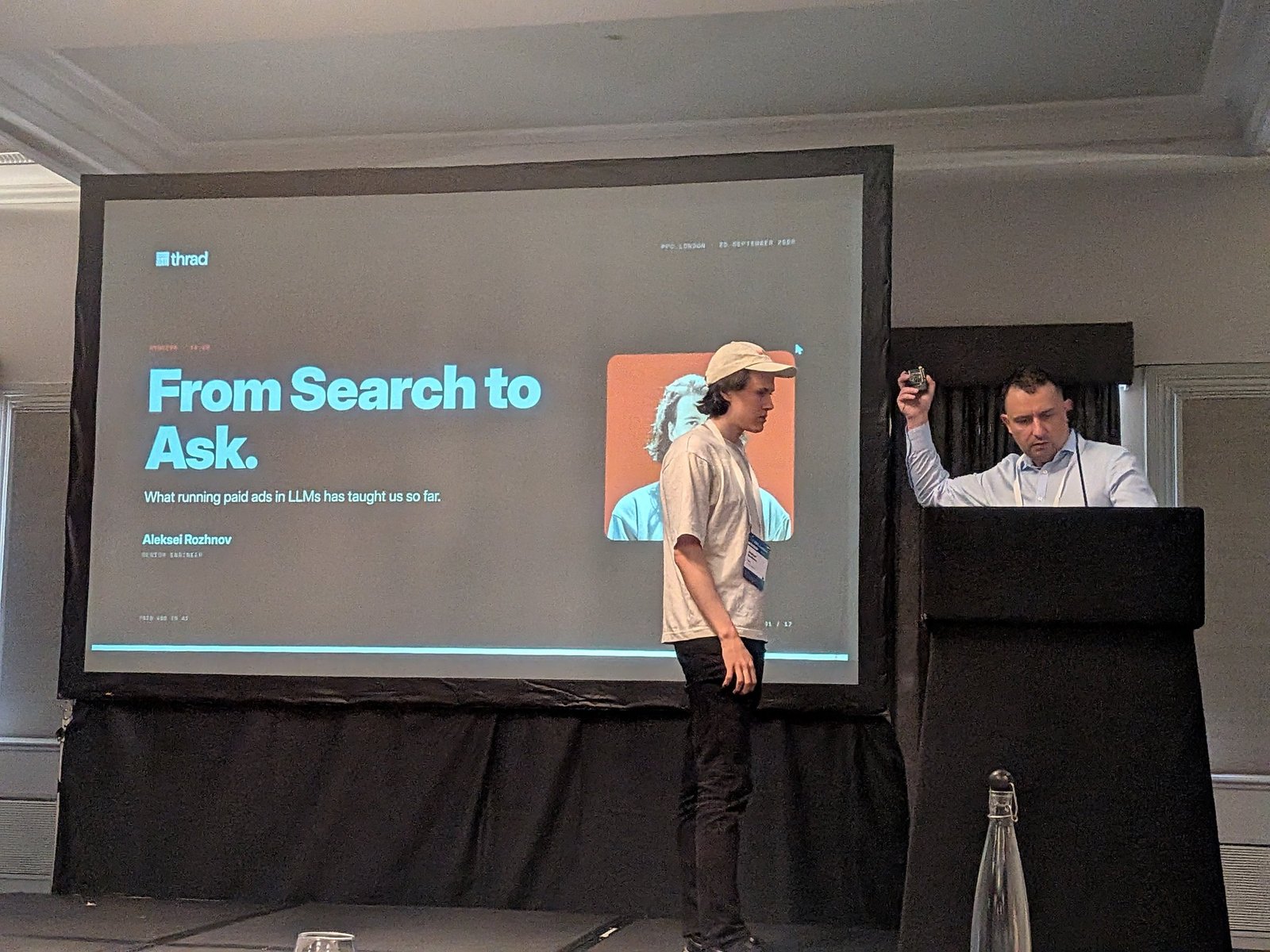 Title slide "From Search to Ask. What running paid ads in LLMs has taught us so far." with Aleksei Rozhnov on stage